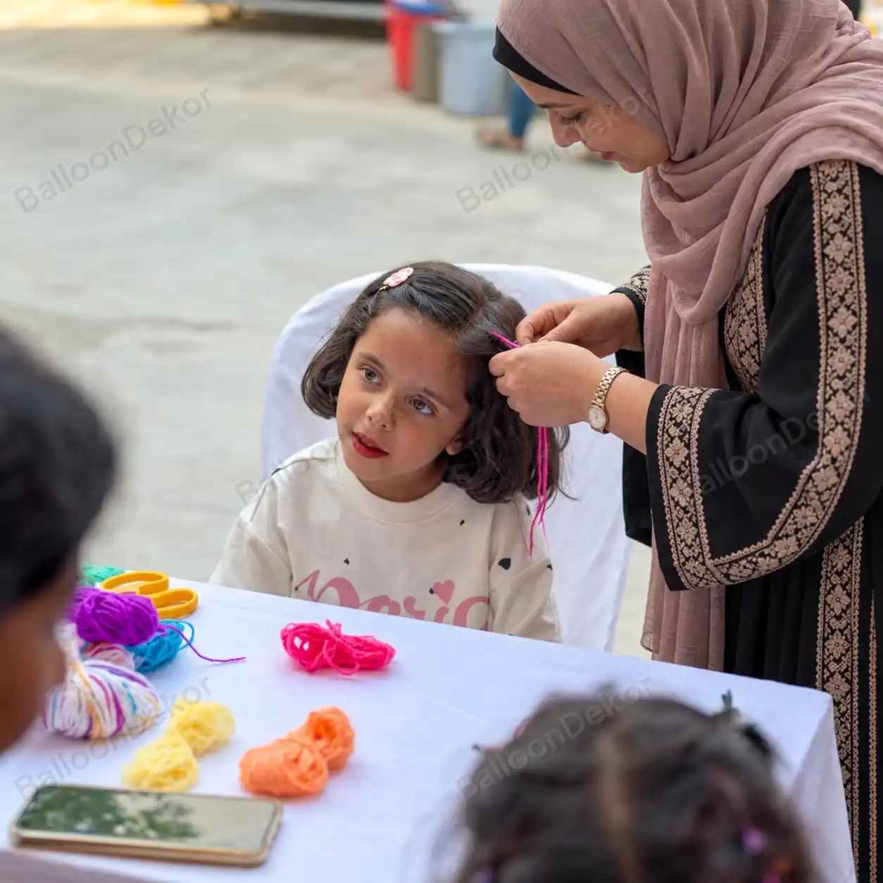 Hair braiding artist adding pink thread to a girl's hair at a kids party table with coloured threads