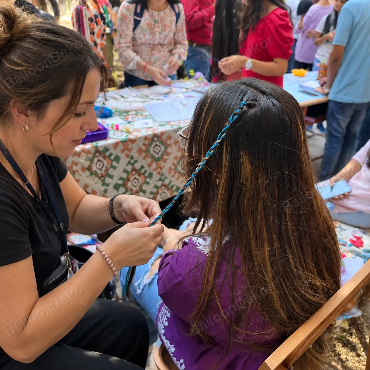 Hair braiding artist weaving a coloured thread braid into a girl's hair at an outdoor kids party in Dubai