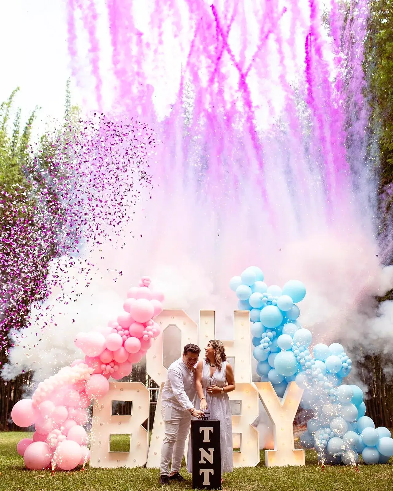 Pink smoke cloud revealing a baby girl behind OH BABY letters at a garden gender reveal