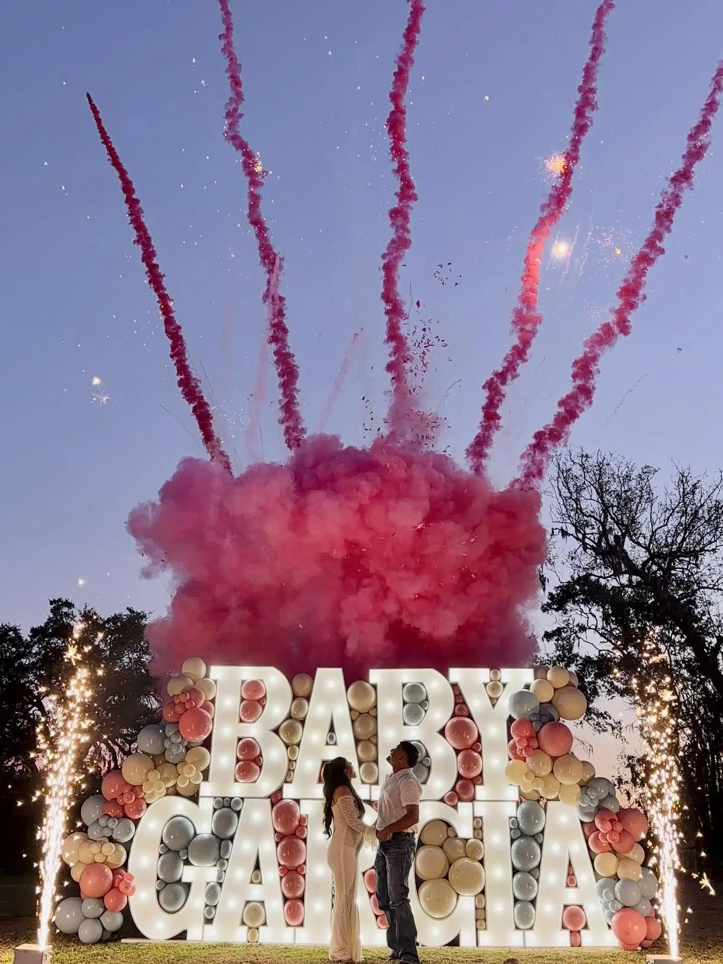 Pink smoke and sparkler reveal above illuminated BABY marquee letters at a night-time gender reveal