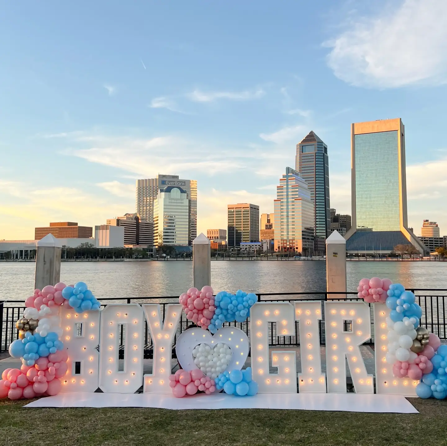 BOY heart GIRL light-up letters with pink and blue balloons at a waterfront gender reveal at sunset